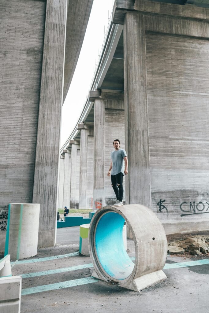 Full length of young man wearing sportswear doing parkour tricks under concrete high bridge