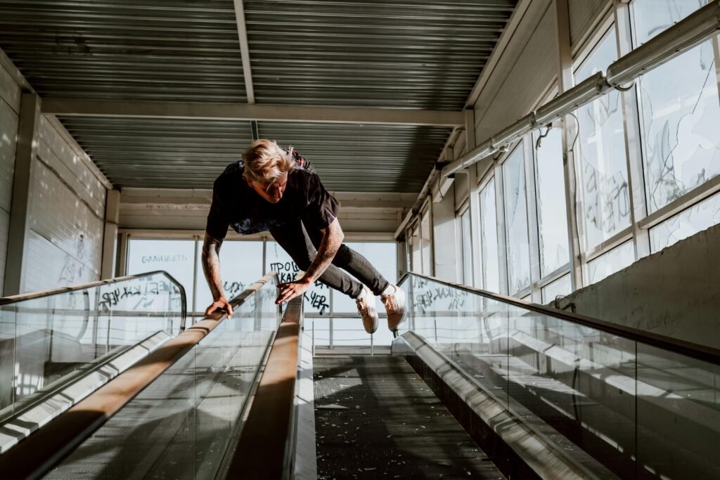 Person performing a parkour stunt on an escalator in an industrial environment with sunlight filtering through windows.