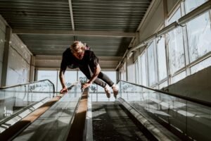 Person performing a parkour stunt on an escalator in an industrial environment with sunlight filtering through windows.