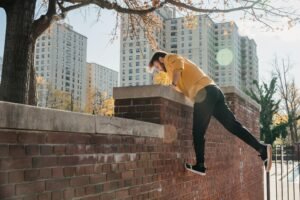 A man gracefully leaps over a brick wall practicing parkour in a cityscape during a sunny autumn day.